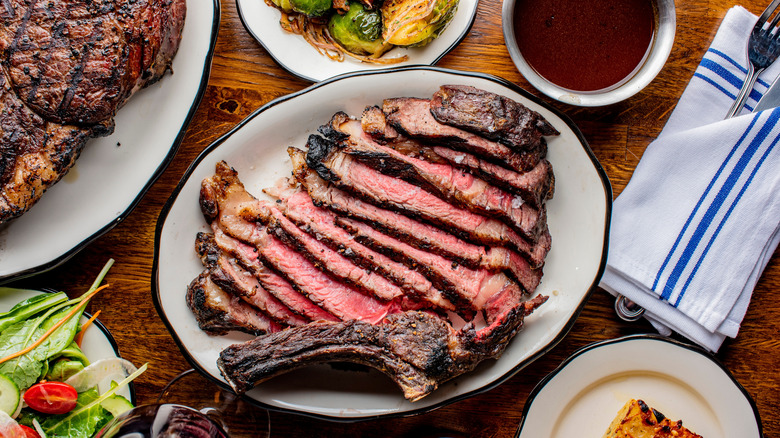 Grilled steak on a white plate, surrounded by side dishes and sauce