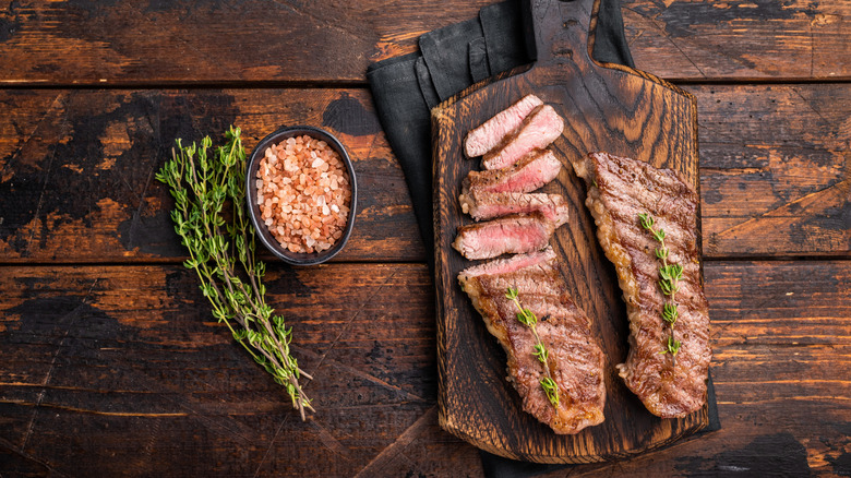An overhead view of grilled tri-tip steaks, with salt and fresh rosemary, served on a wooden board