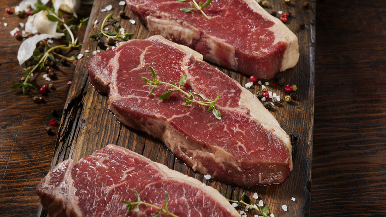 A wooden board with seasoned steaks