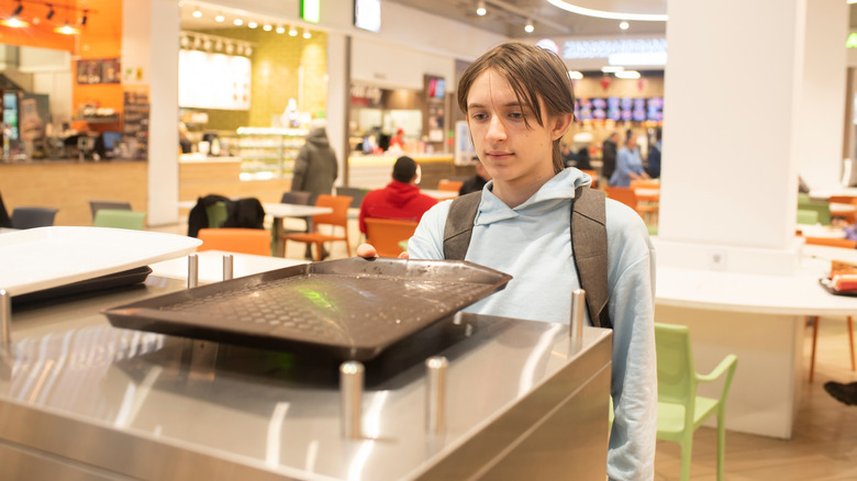 A teenage boy returns a tray in a mall food court