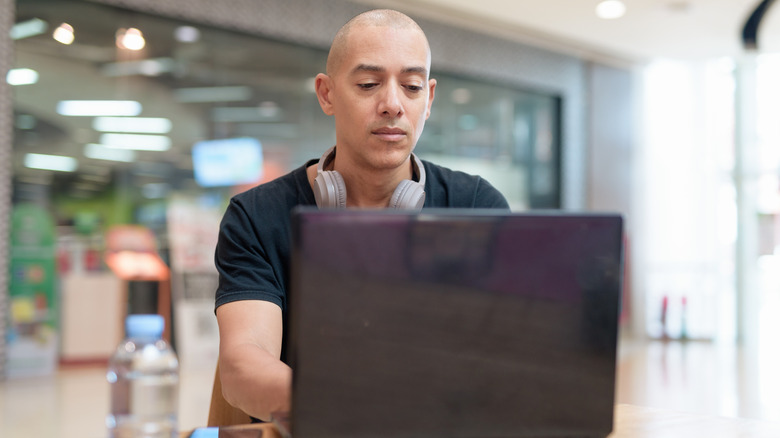 A man works on his laptop in a food court