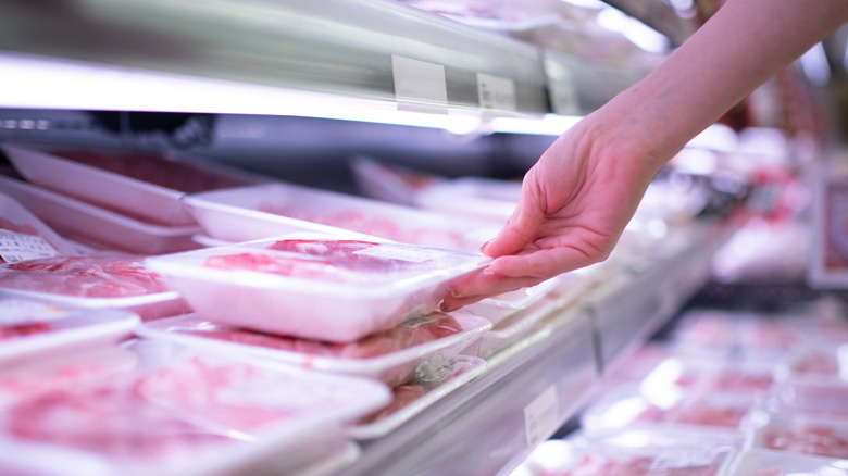 A person picks up a pack of meat in a supermarket