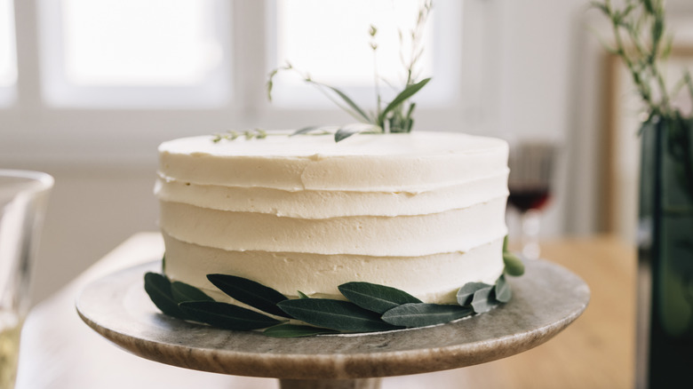 A white frosted cake decorated wtih fresh greenery