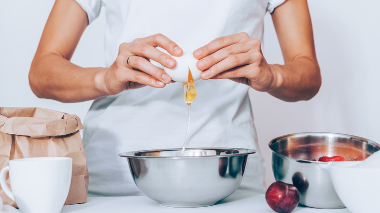 A person carefully cracks an egg over a metal bowl