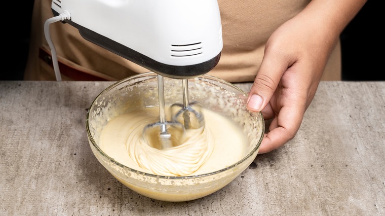 A person uses a hand mixer to mix a small bowl of cake batter