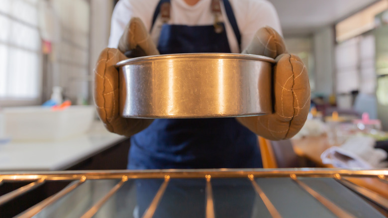 A person places a round metal cake pan into the oven