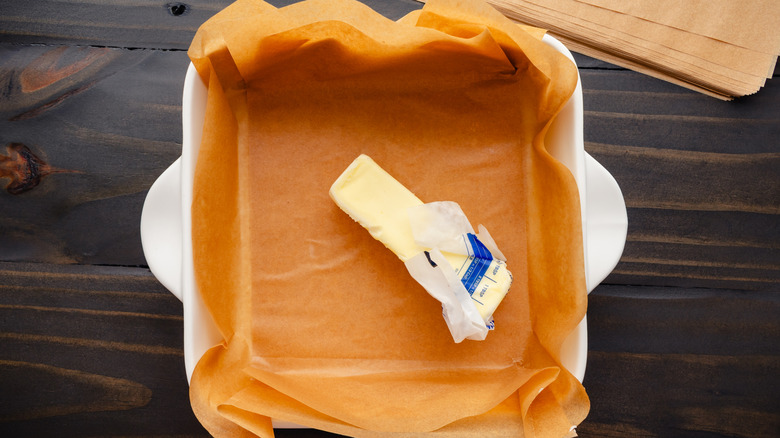 A stick of butter sits in a lined ceramic pan
