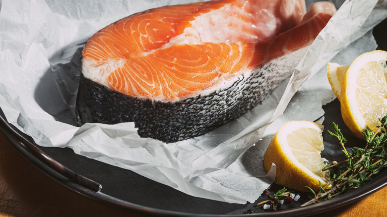 Raw salmon steak and lemons in a pan lined with parchment paper