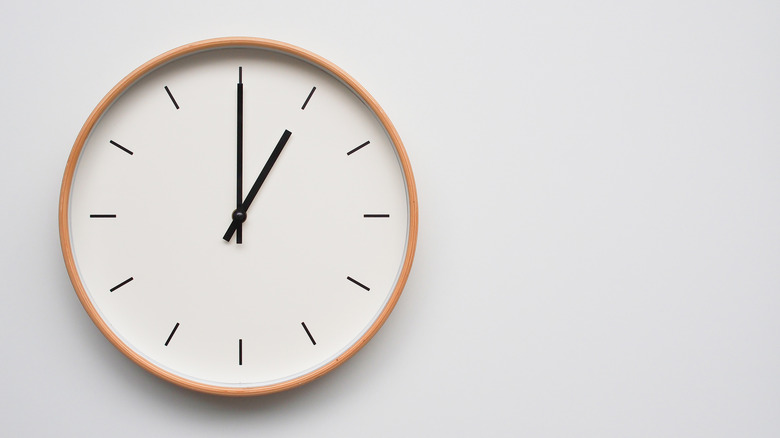 A white minimalist clock, with the hands pointed to one o'clock