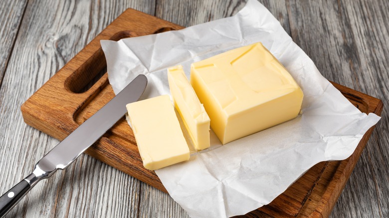 Butter sits unwrapped on a wooden cutting board against a wooden surface