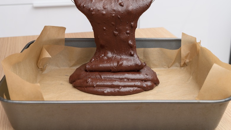 Brownie batter being poured into a metal baking pan that's been prepared with a liner
