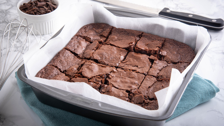 Chocolate brownies in a steel pan that are crumbling because they were cut too soon