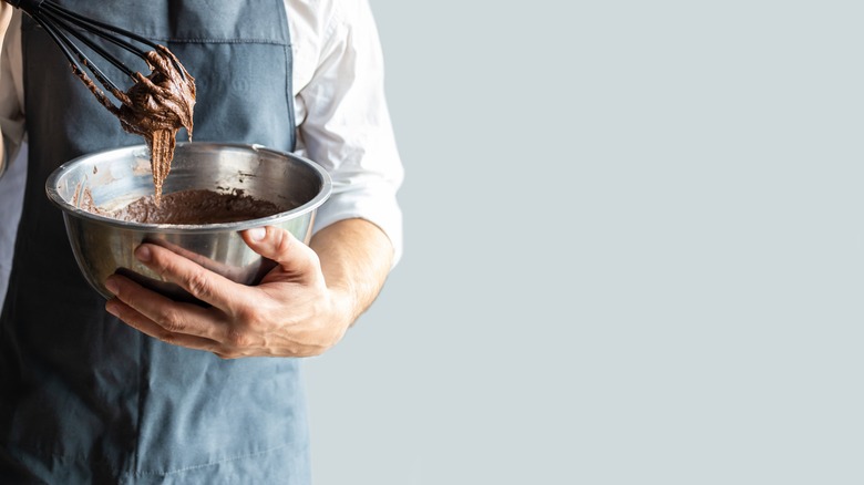 A person mixing brownie batter with a whisk against a bright blue background