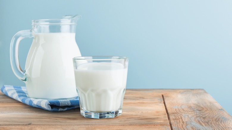 A jug of milk and a glass of milk on a wooden surface against a blue background