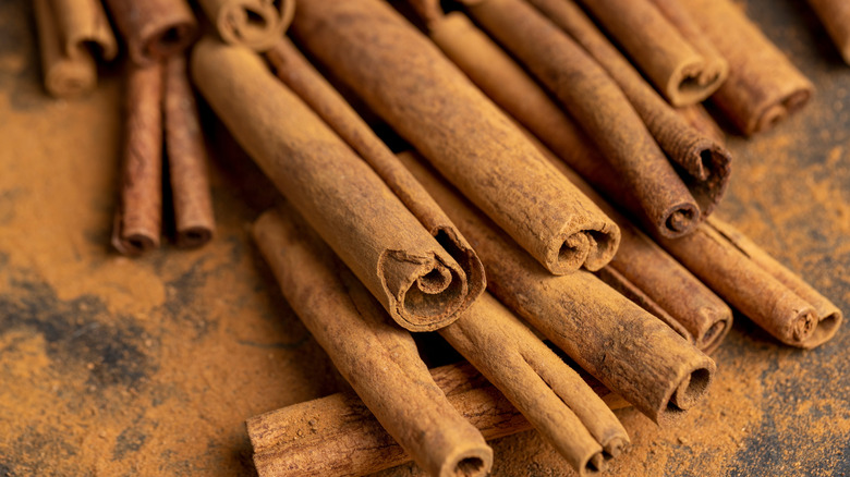 Cinnamon sticks on a black plate covered in brown powder