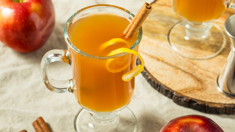 Orange liquid (hot toddy) in a glass with cinnamon and orange peel.