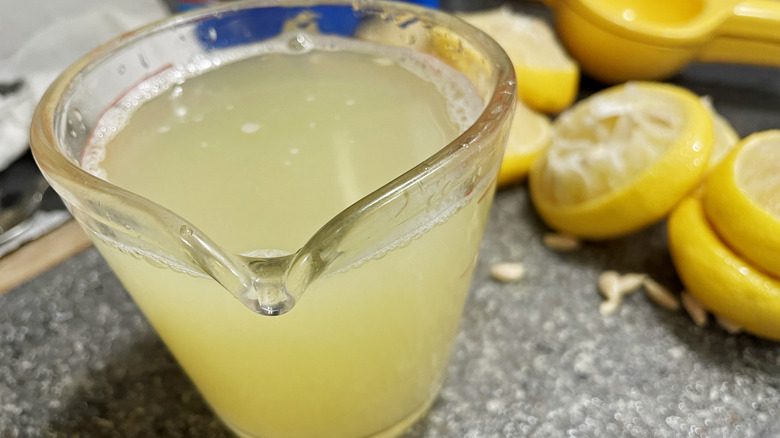 A jug of fresh lemon juice, with juiced lemons behind it