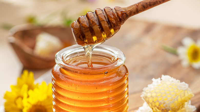Honey drizzles from a honey dipper into a jar