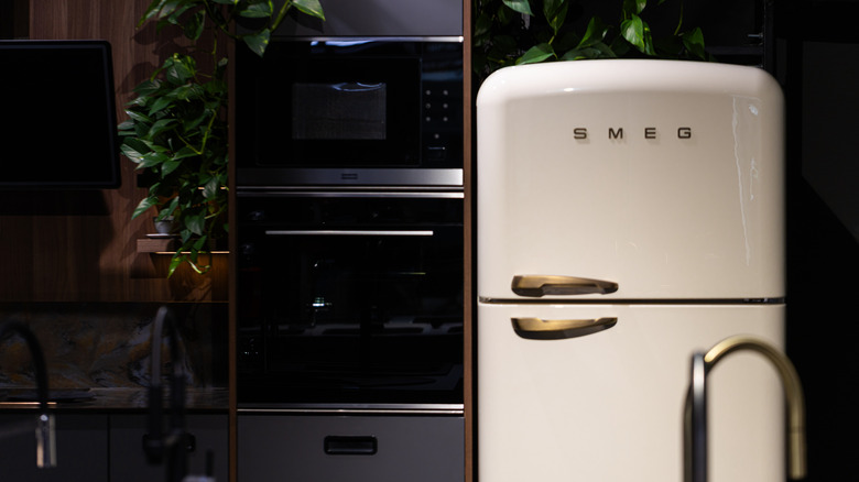 A SMEG refrigerator sits in a modern kitchen, next to a built-in oven and microwave