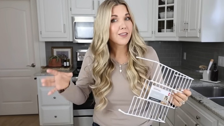 A woman in a kitchen, holding a wire step storage rack