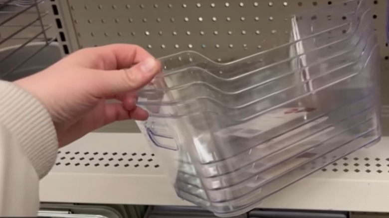A woman picking up a stack of clear plastic refrigerator food storage bins