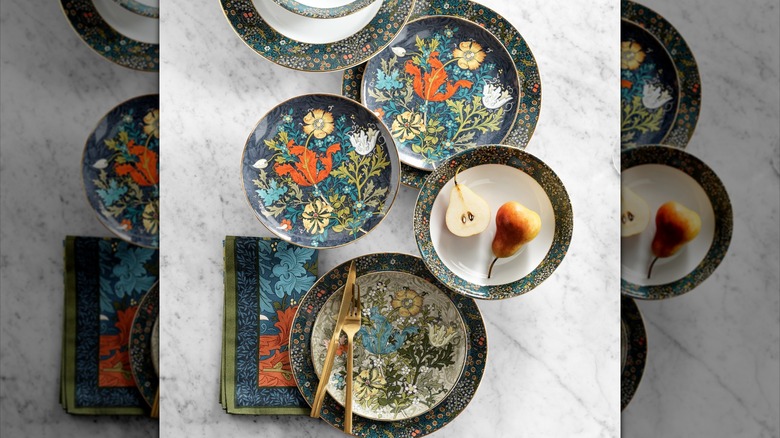 Assorted plates with colorful, floral arts-and-crafts designs, with complementary napkins and gold flatware