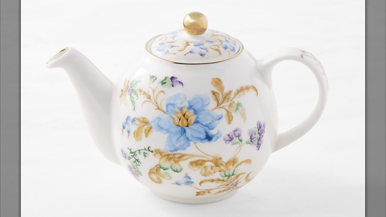 A white teapot decorated with blue, purple, and yellow floral designs