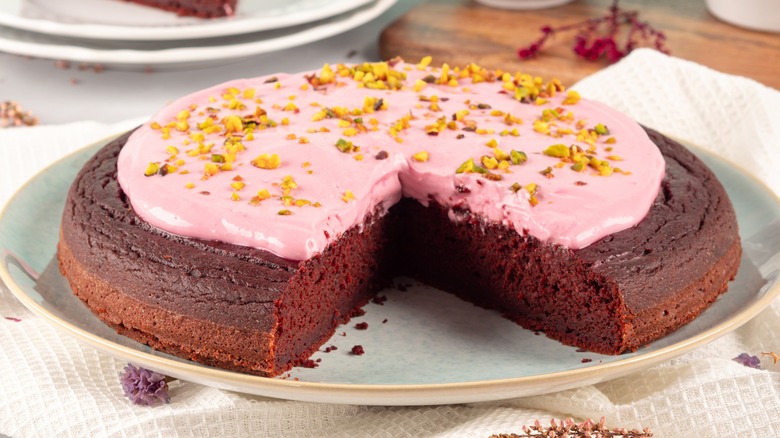Cake with pink cream cheese icing sprinkled with nuts on top