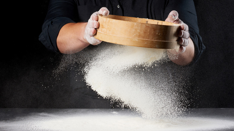 A person uses a sifter to sift a white powder onto a table