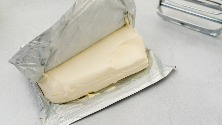 A block of white cream cheese with its foil packaging partially unwrapped