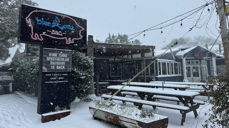 Exterior and seating area with sign for Blue Oak BBQ covered in snow