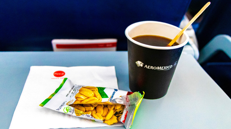 A packet of peanuts and a black coffee are served on an airplane