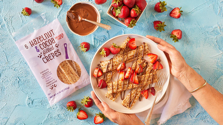 Hands holding plate of hazelnut and Cocoa Filled Crepes with strawberries and chocolate