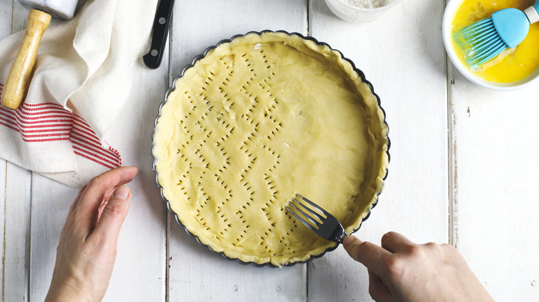 A baker pricks holes in their pie crust