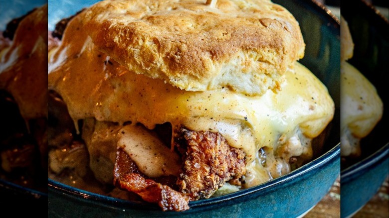 A fried chicken sandwich with melted cheese, bacon, and sausage in a blue dish
