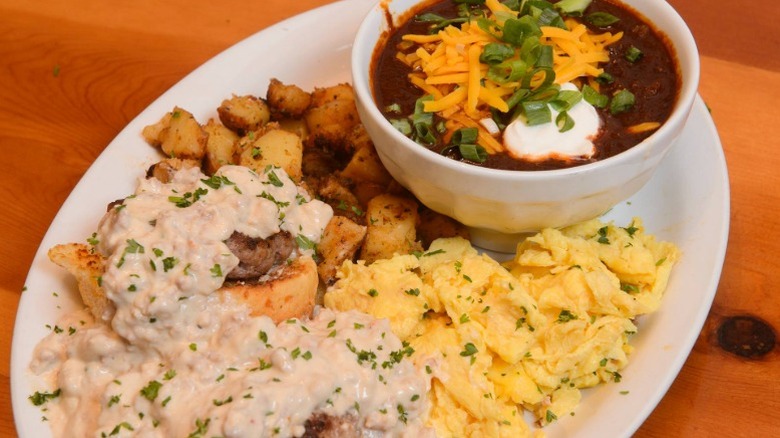 A plate of biscuits and gravy with potato, Cheddar, sauce, and scrambled egg