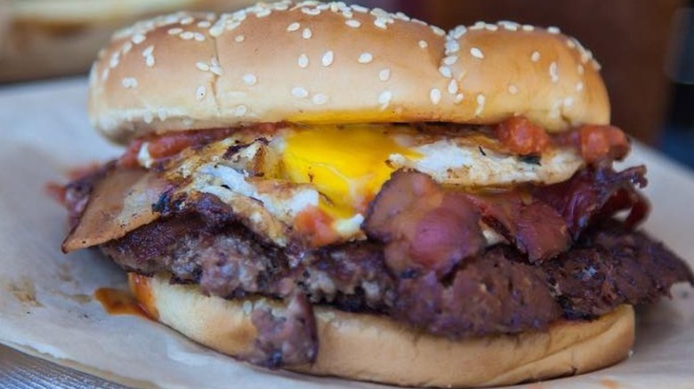 A hamburger in a sesame burger bun with bacon and eggs