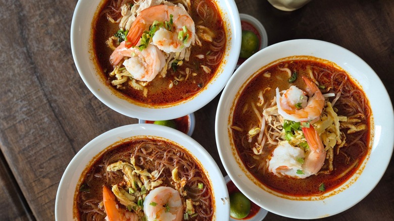 Three bowls of Sarawak laksa topped with shrimp on wooden table