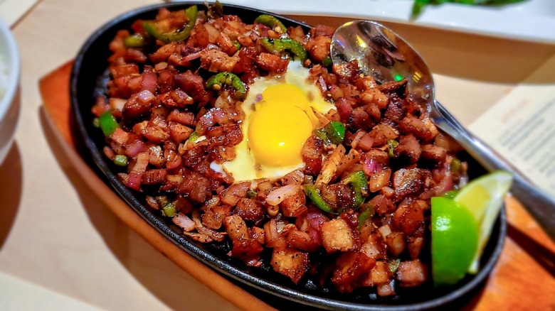 Iron skillet of sigsig topped with runny egg and lime