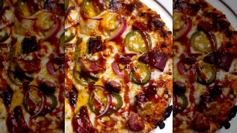 BBQ sauce is drizzled on a pizza with brisket, onions, and jalepenos