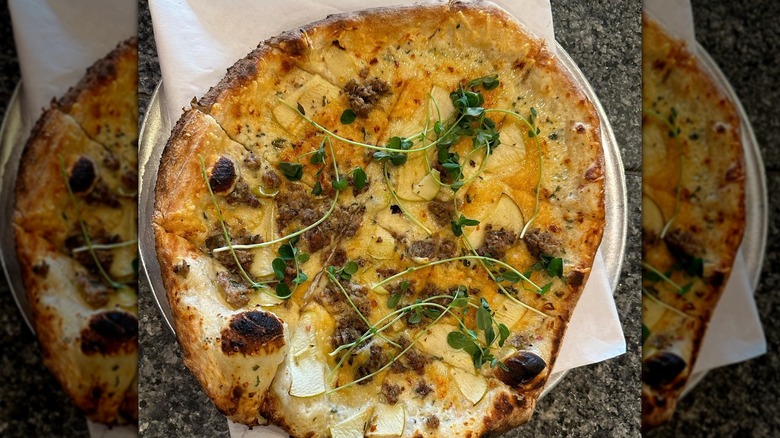Pizza topped with apples, sausage, and microgreens
