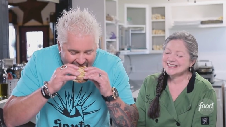 Guy Fieri takes a bite out of a meatloaf panini at Joy's Once Upon A Thyme, while chef Joy Templeton looks on smiling