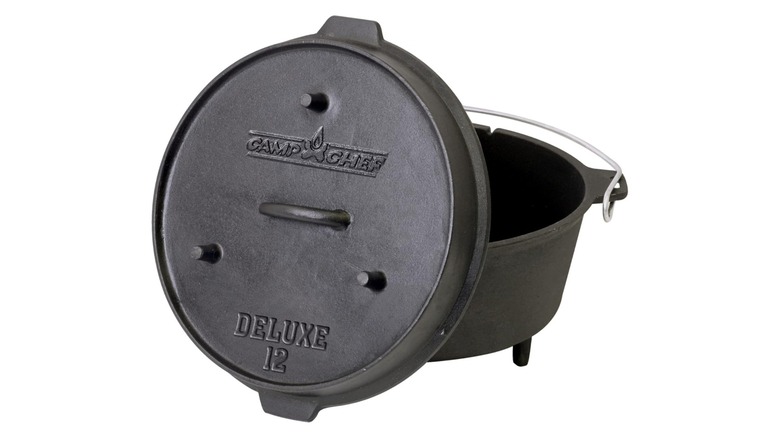 A black Camp Chef Dutch oven with stubby feet on the oven and lid; the lid has the company logo and says "Deluxe 12" and everything is sitting against a white background.