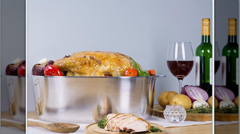 A MAGNAWARE aluminum Dutch oven with a roasted turkey inside with sliced turkey, red wine, and vegetables on the table.