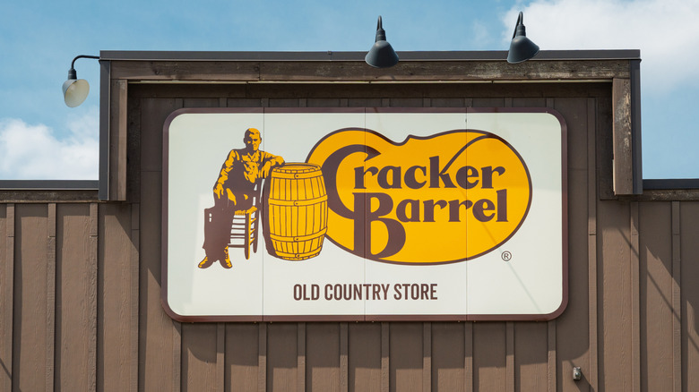 A Cracker Barrel store logo on the exterior of a restaurant, blue sky in the background.