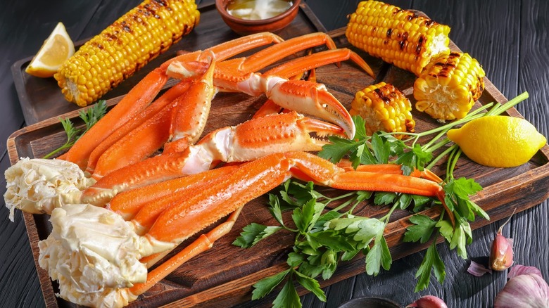 Crab legs on a cutting board with corn on the cob, lemons, and parsley