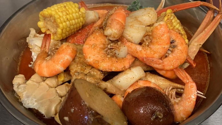 A closeup of a seafood boil at Sexy Crab featuring shellfish, potatoes, and corn in a silver bowl