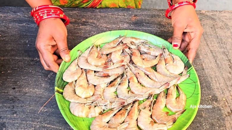 A woman holds a plate of whole, unshelled prawns, in a still from an Aja Kitchen YouTube video