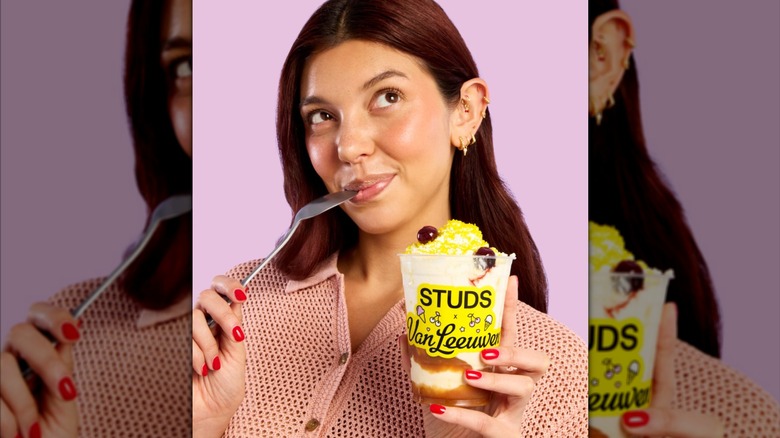 a woman wearing diamond huggy earrings, holding a studs x van leeuwen sundae, posing with a spoon to her lips