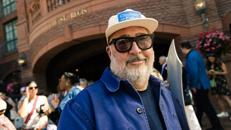 a bearded Ander Zimmern stands outside with a white hate and sunglasses